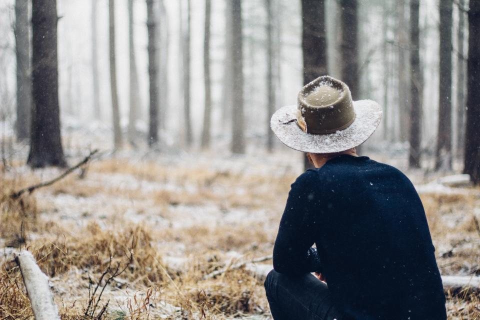 A man in a wide brimmed hat crouched in a frosty forest